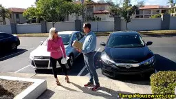 Blondine in pinker Bluse wartet neben weißem Sportwagen.