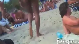 Nacktes Paar kniet auf buntem Handtuch, Sonnenbader im Hintergrund